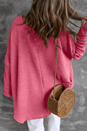 Asymmetric slouch knit top in strawberry acrylic with a relaxed fit and long sleeves.
