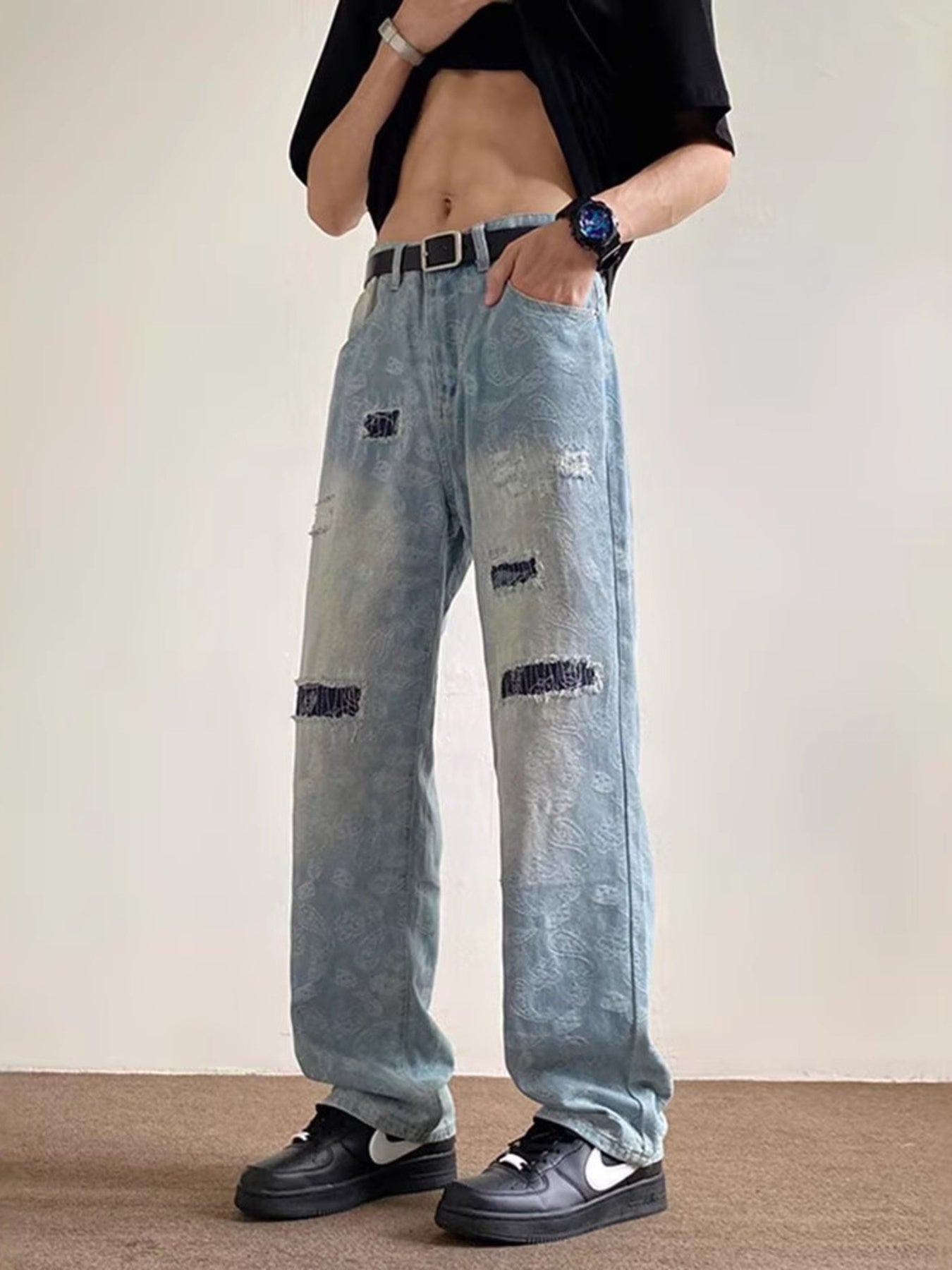 Men's light blue distressed wide-leg jeans with paisley pattern and pocket details.
