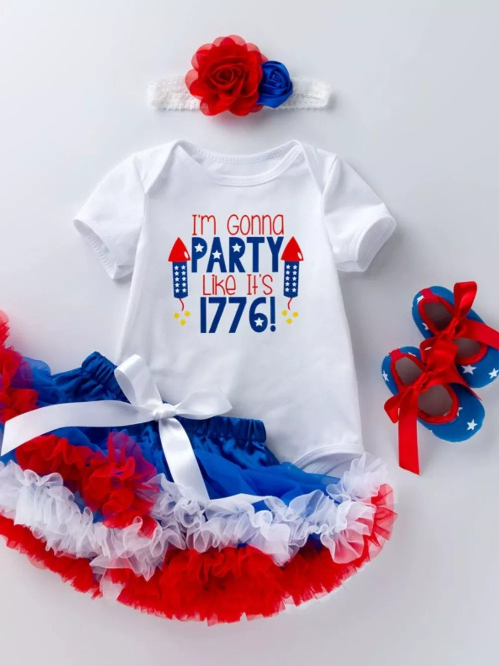 White baby onesie with "I'm Gonna Party Like It's 1776!" text, red & blue tutu, headband, and star shoes.