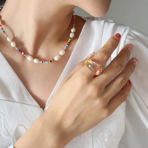 Gold choker with baroque pearls and colorful seed beads, styled with a clear floral ring.