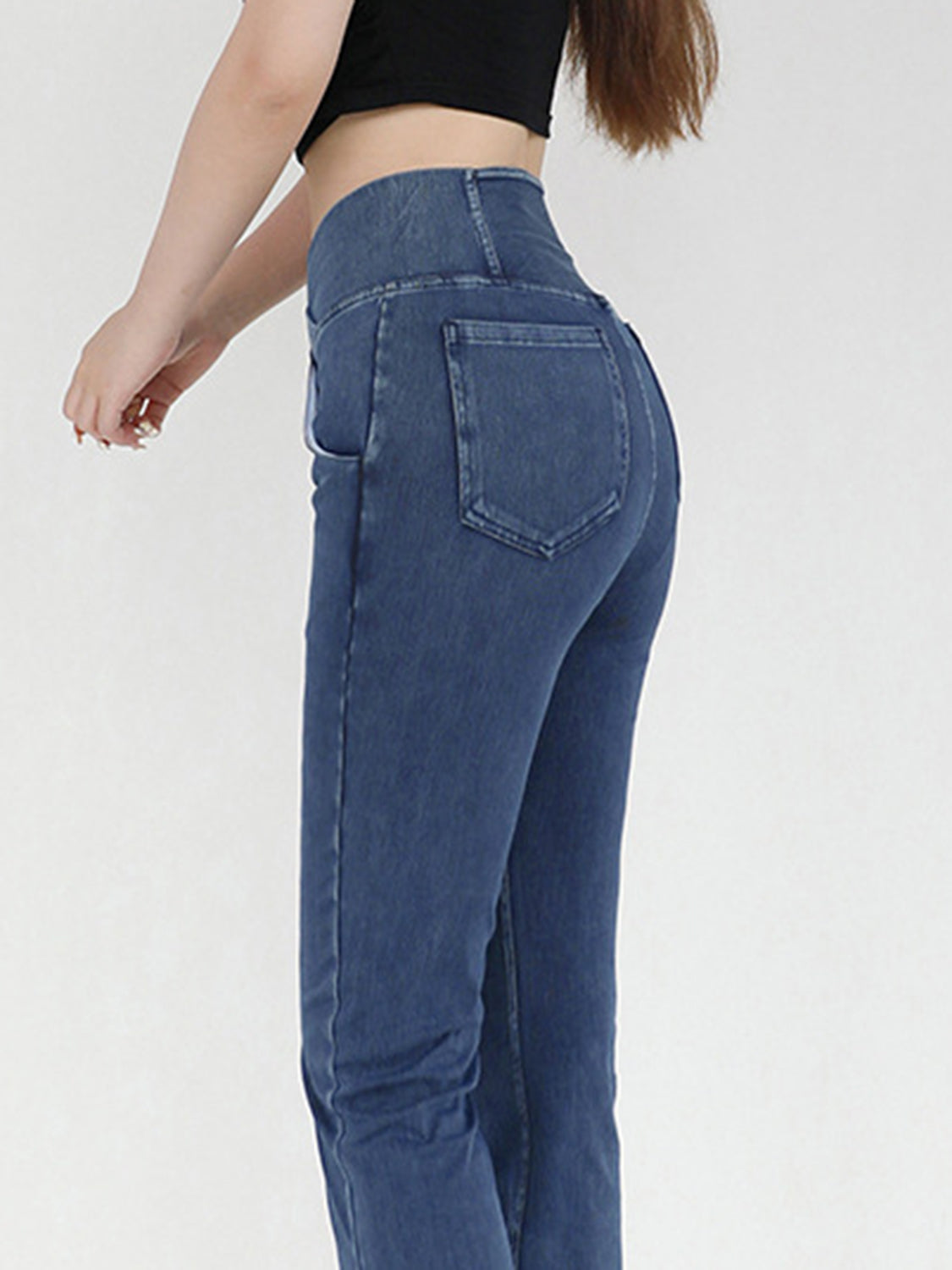Medium wash denim jeans with crossover waist and flare leg, detailed view of back pockets.