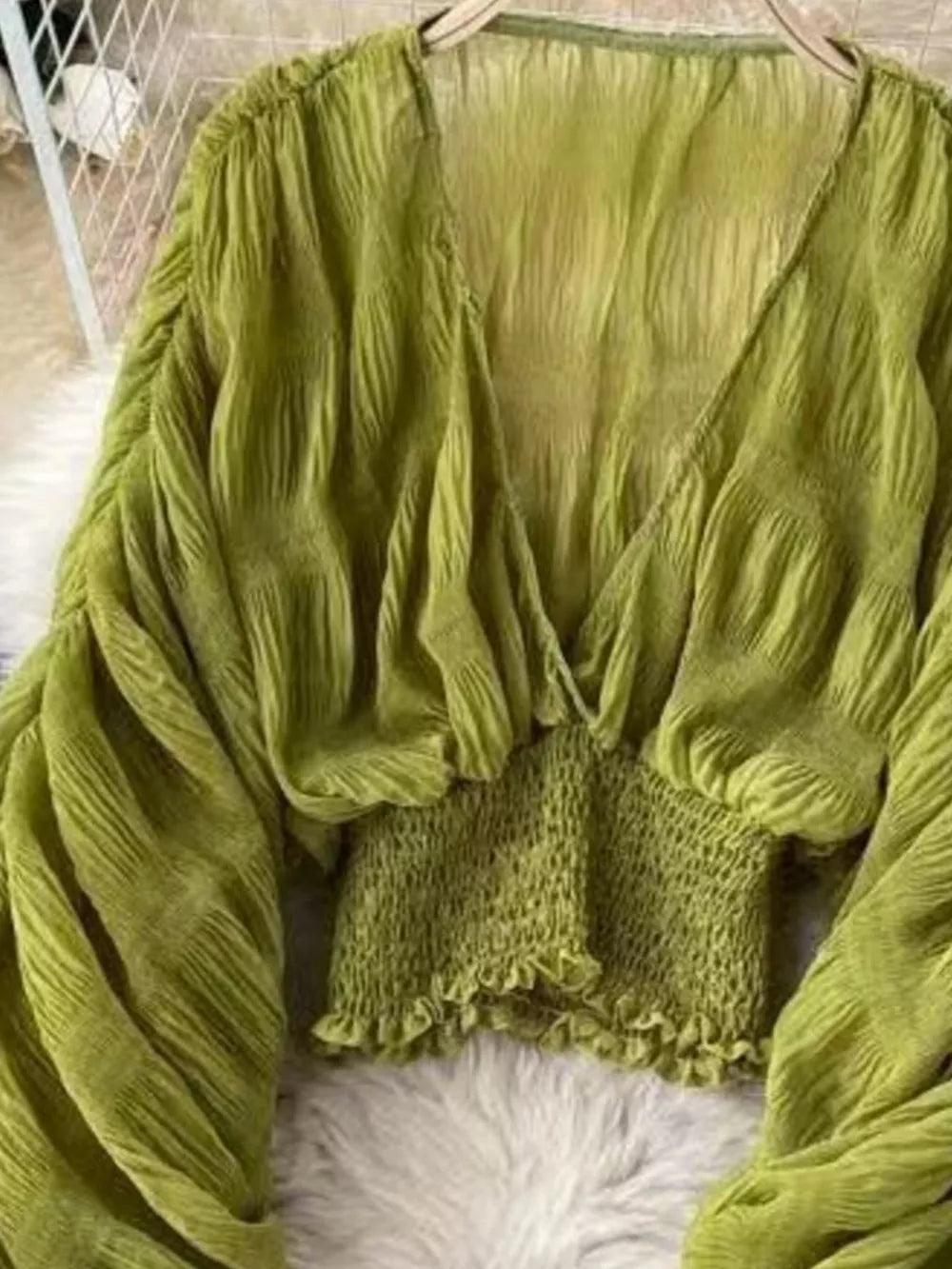 Green ruched sleeve blouse with deep V-neck and smocked waist detail.