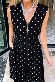 Black polka dot midi dress with zipper, smocked waist, and ruffled neckline detail.