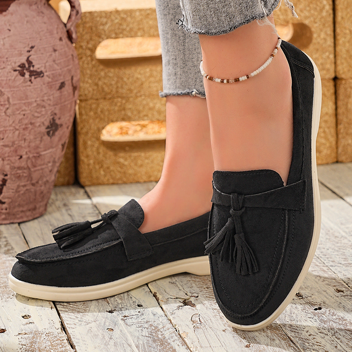 Black faux-suede slip-on loafers with decorative tassels and a bow detail.