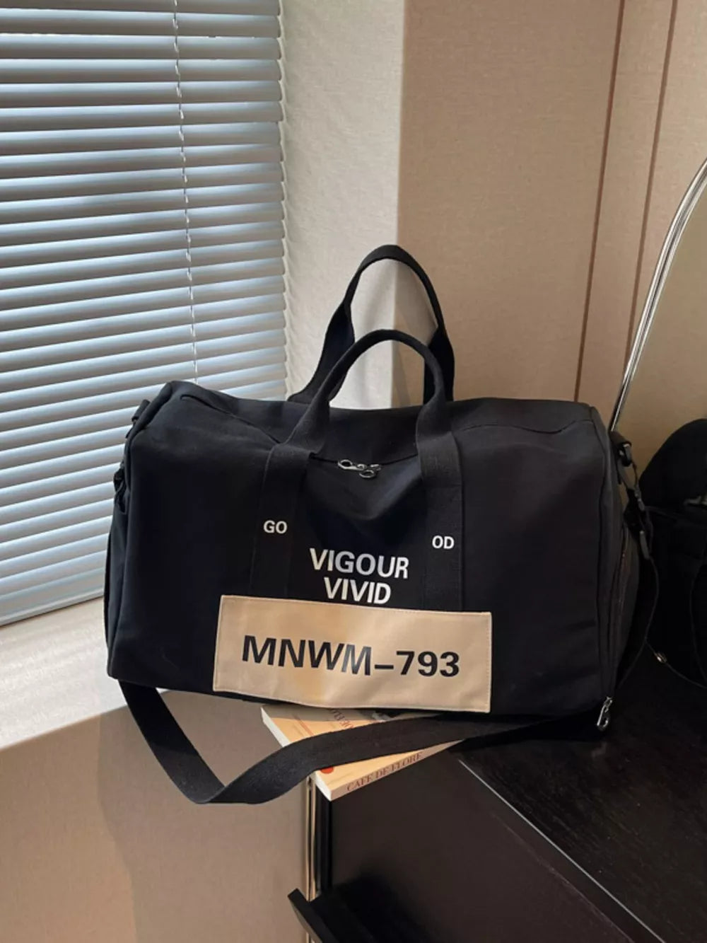 Black nylon travel bag with "Vigour Vivid" print and strap.