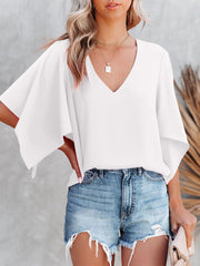 White V-neck blouse with wide flutter sleeves, styled with denim shorts.