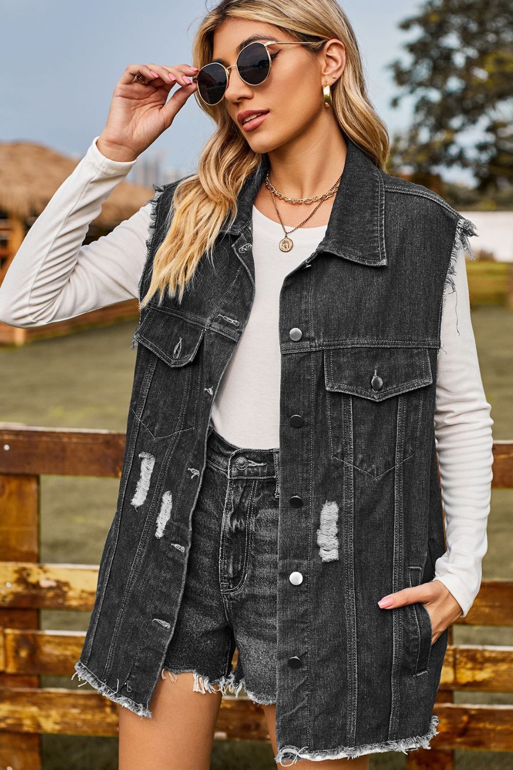 Dark distressed denim sleeveless jacket with frayed hem and button front.