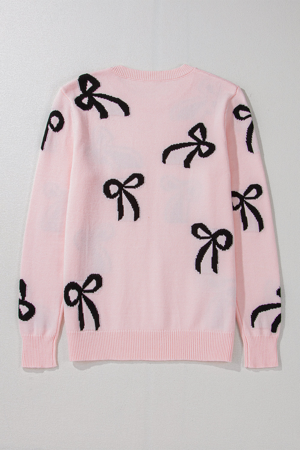 Blush pink knit crewneck sweater with allover black bow motifs.