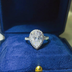 White pear-cut halo engagement ring with pave band in a blue box