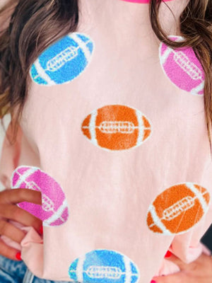 Pink t-shirt with all-over football appliqué pattern in blue, orange, and pink.