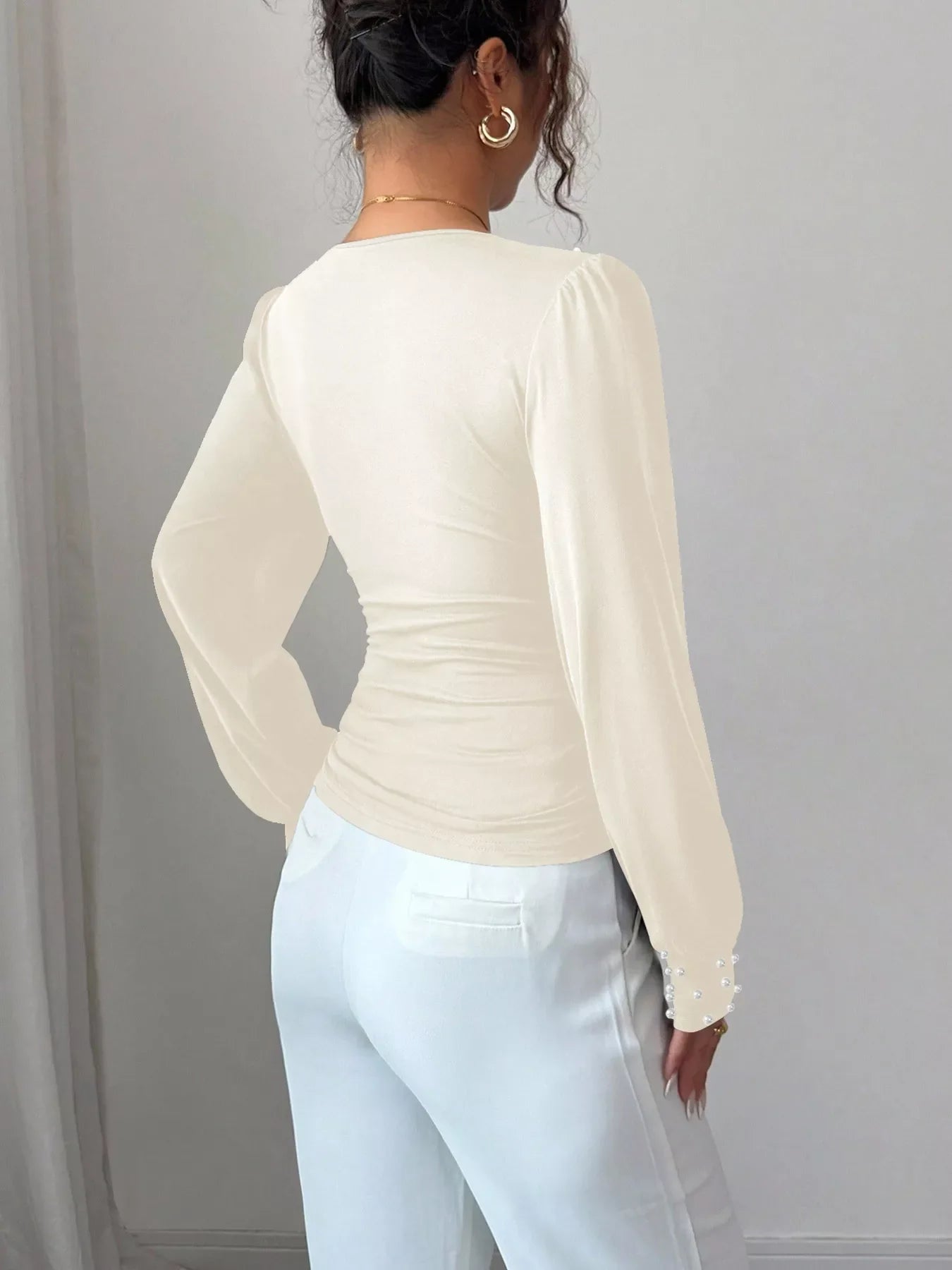 Beige ruched V-neck blouse with pearl embellished cuffs and long sleeves.
