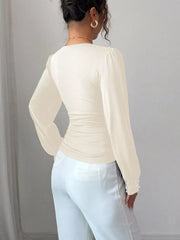 Beige ruched V-neck blouse with pearl embellished cuffs and long sleeves.
