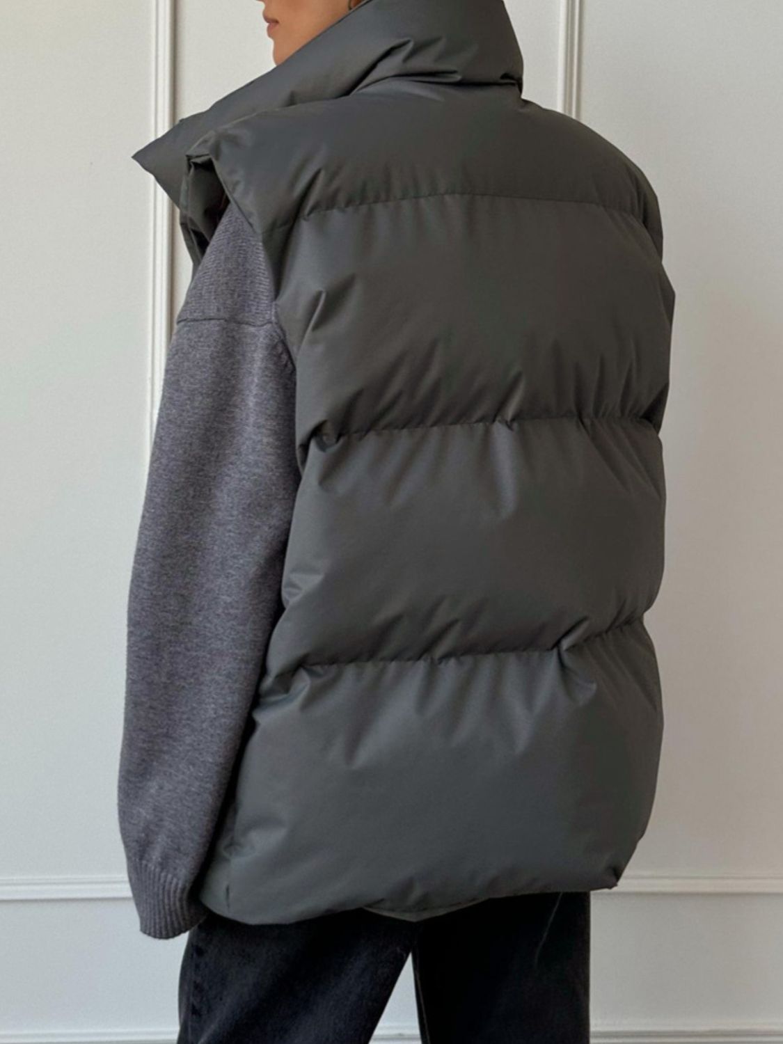 Padded puffer vest in Dark Gray with a high collar, shown layered over a gray sweater.