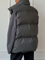Padded puffer vest in Dark Gray with a high collar, shown layered over a gray sweater.