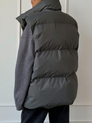 Padded puffer vest in Dark Gray with a high collar, shown layered over a gray sweater.
