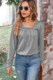 Gray long sleeve top with square neckline and front pleats, styled with jeans.