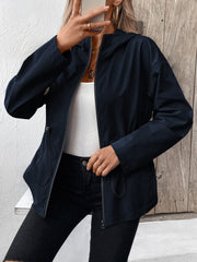 Navy utility jacket with cinched waistline, hood, and zip front, styled with a white tank and black jeans.