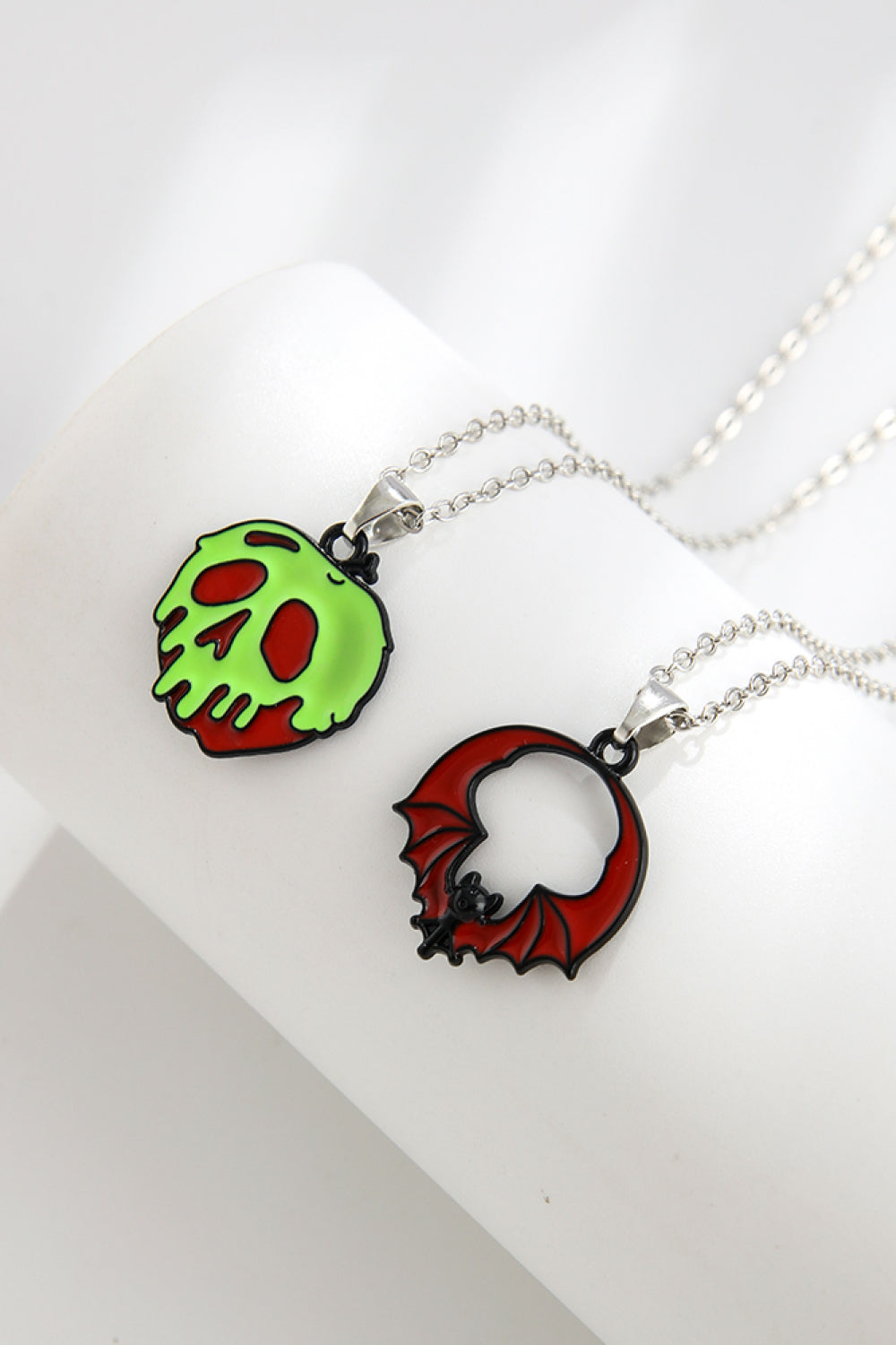 Spooky season enamel pendant necklaces, one green skull, one red bat.
