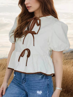 White peplum shirt with puff sleeves, brown trim, and tie details.
