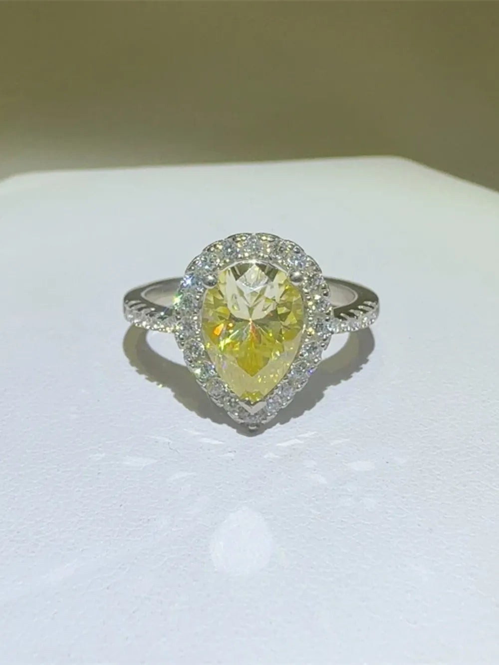 Yellow pear-cut moissanite ring with diamond halo and textured band.