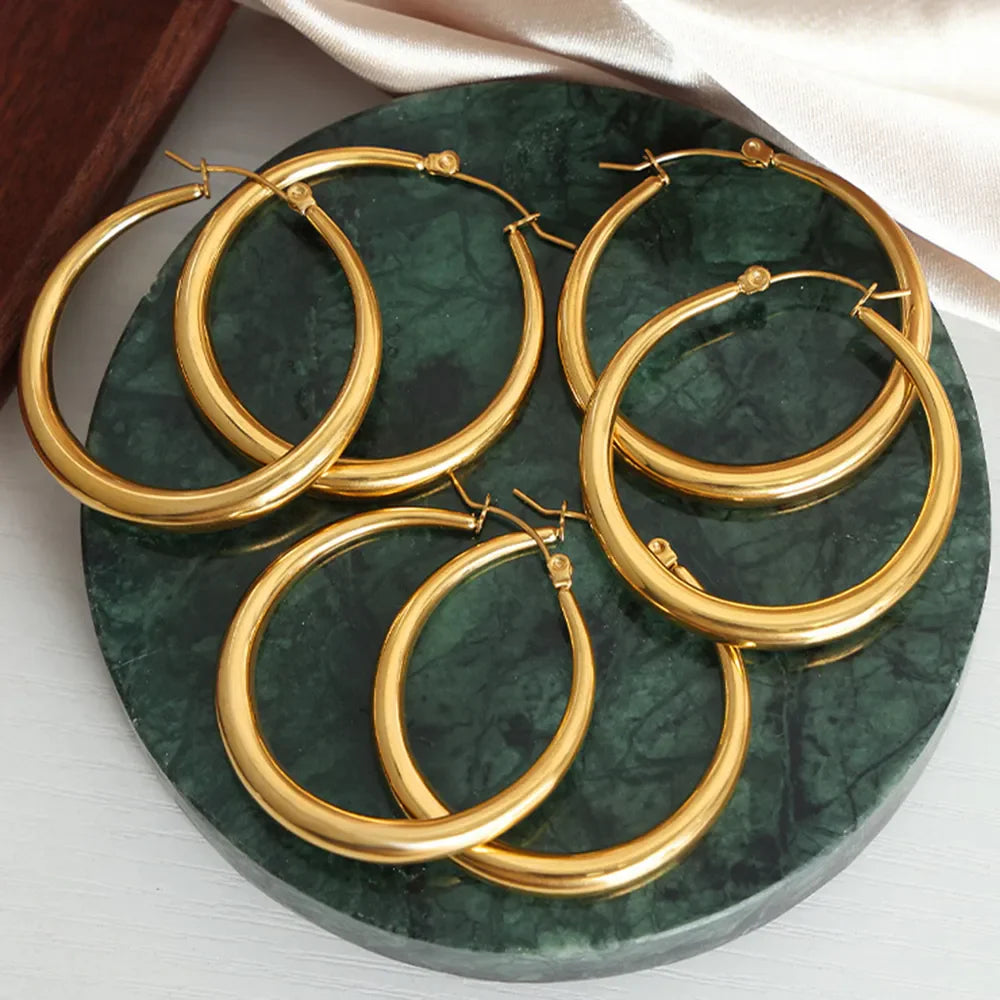 Sculpted oval gold hoop earrings, 18K gold-plated, displayed on a green marble surface.