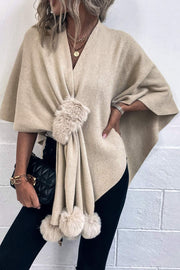 Taupe knit cape with fur trim and pom-poms, V-neck, draped silhouette.