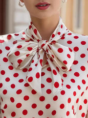 White polka dot shirt with a large red bow tie neck and cap sleeves.