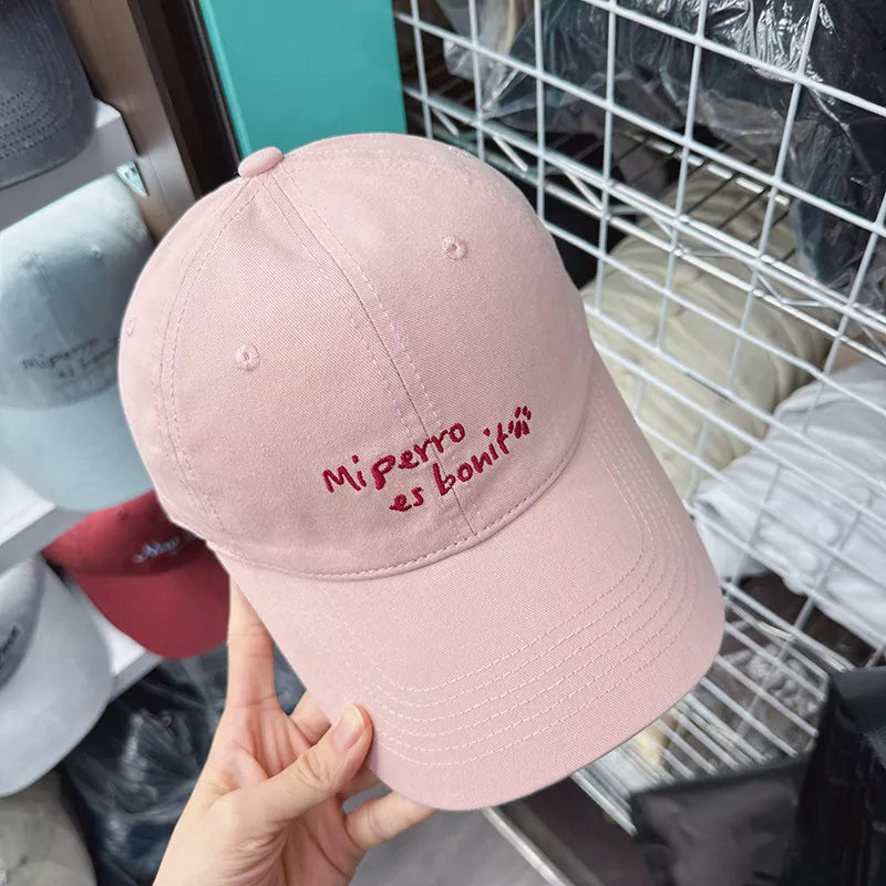 Pink baseball cap with embroidered "Mi perro es boniti" text and paw print detail.
