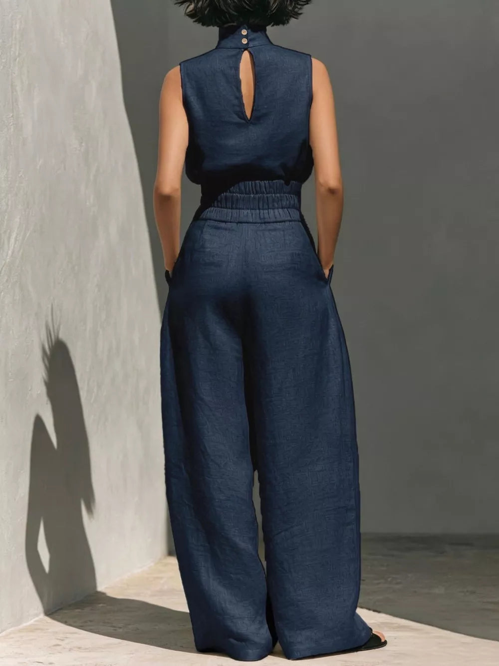 Navy blue sleeveless turtleneck set with buttoned keyhole back and wide-leg pants.