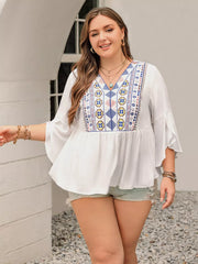 White plus size shirt with vibrant geometric embroidery, V-neck, and bell sleeves.