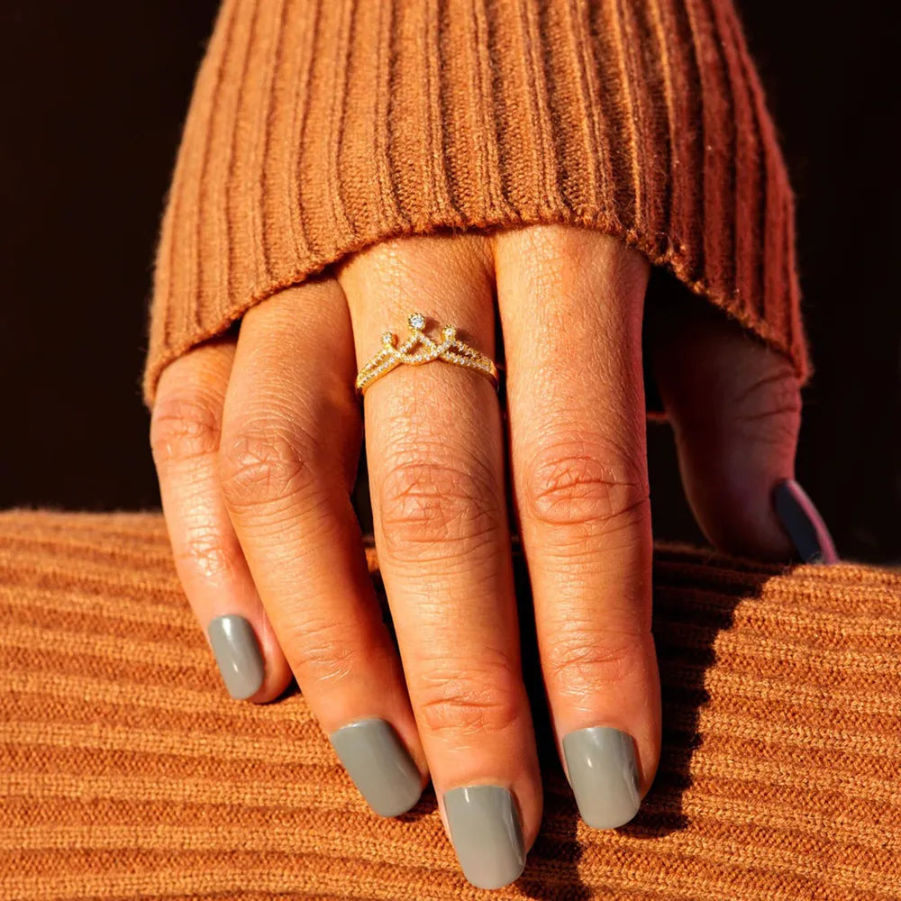 Gold pave crown ring with small diamonds on a hand wearing a brown sweater.