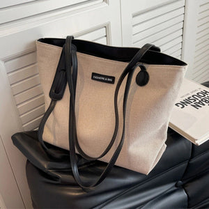 Large canvas shoulder bag in beige with black leather trim and straps.