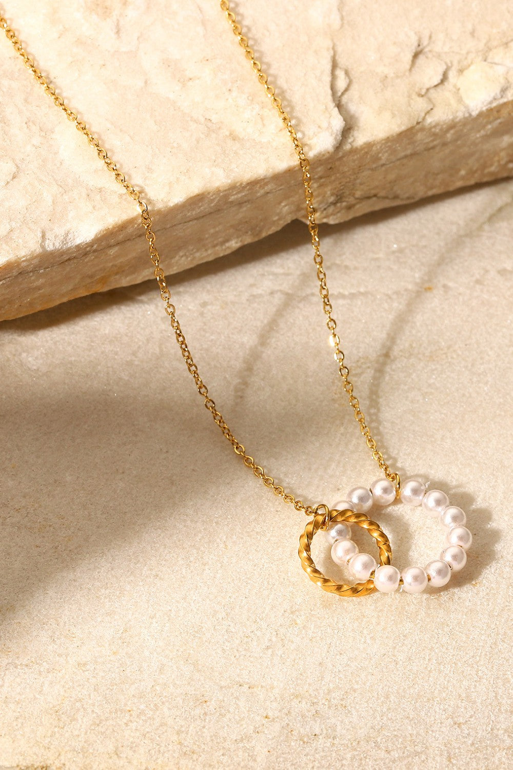 Gold-plated necklace with interlocking pearl and twisted circle pendants.