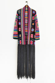 Granny square crochet duster with black fringe, open front, long sleeves, and colorful boho pattern.