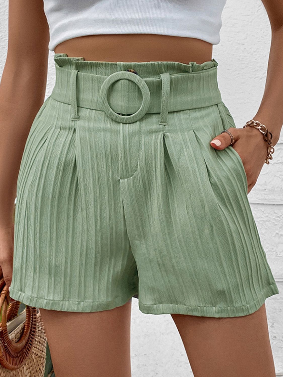 Light green pleated high-waist belted bermuda shorts with a ring buckle and vertical stripe texture.