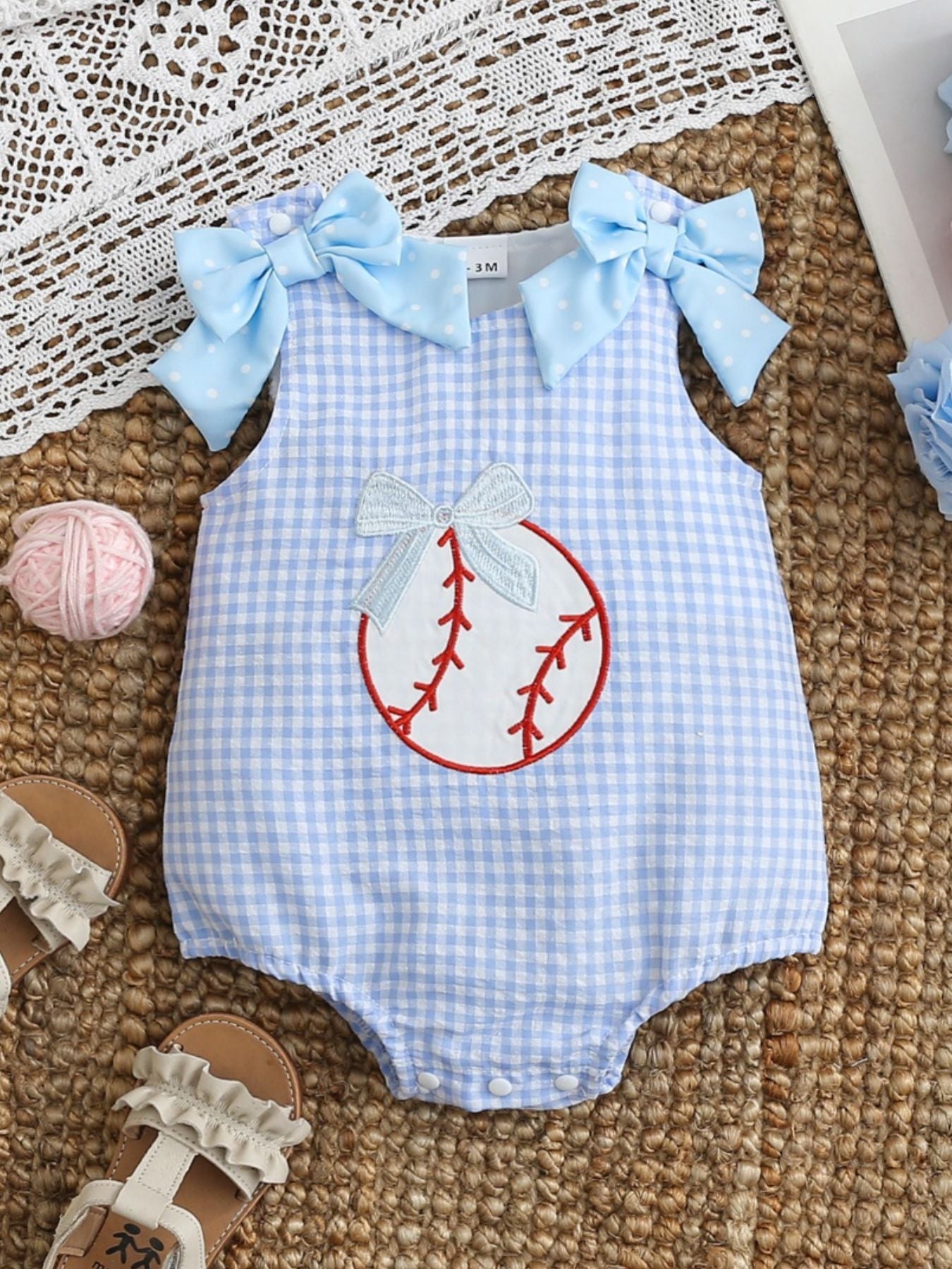 Baby one-piece in pastel blue gingham with baseball embroidery and bow details