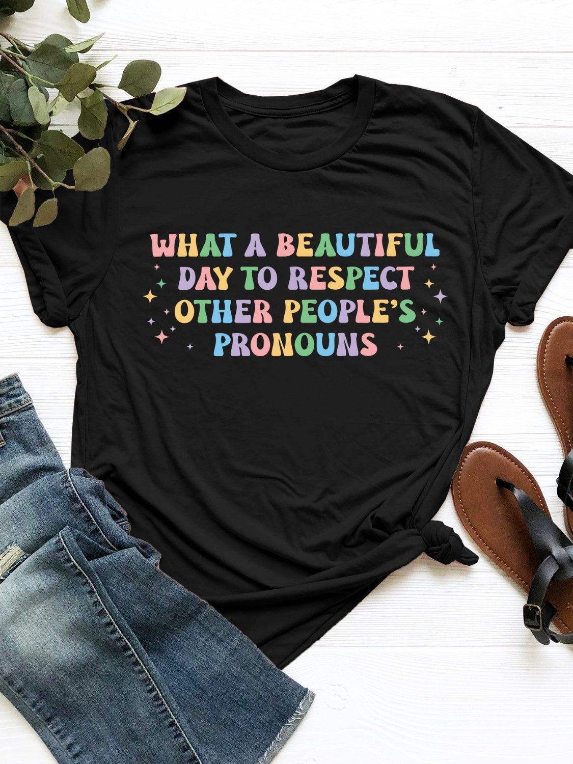 Black polyester t-shirt with "What a beautiful day to respect other people's pronouns" graphic in pastel colors.