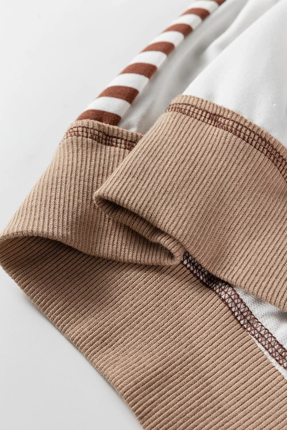Beige sweatshirt detail with contrast stitching and striped sleeve cuff