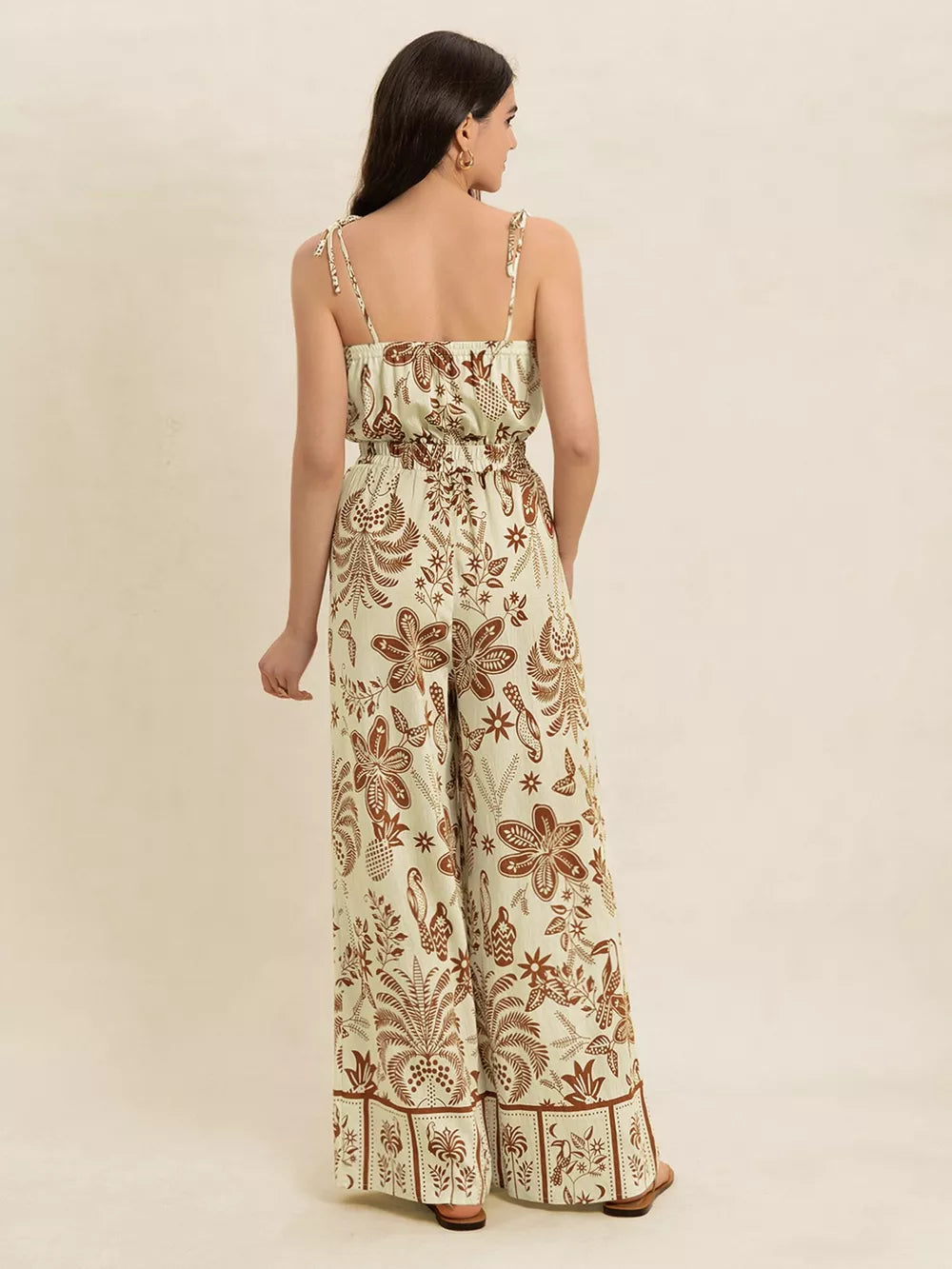 Tropical tie strap wide-leg romper in cream with brown floral print, smocked waist, and tie straps.