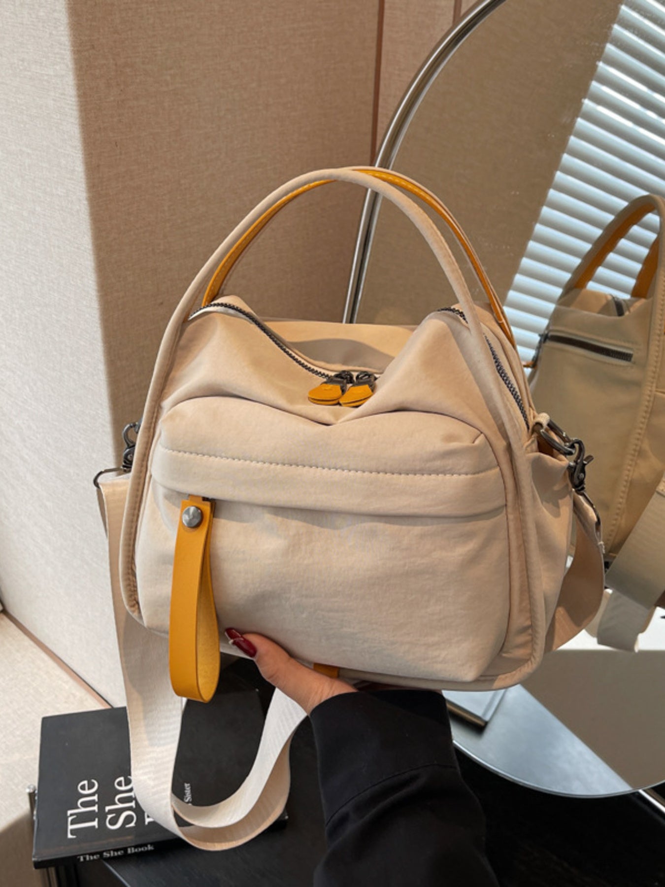 Khaki crossbody bag with yellow pull tab detail and adjustable strap.