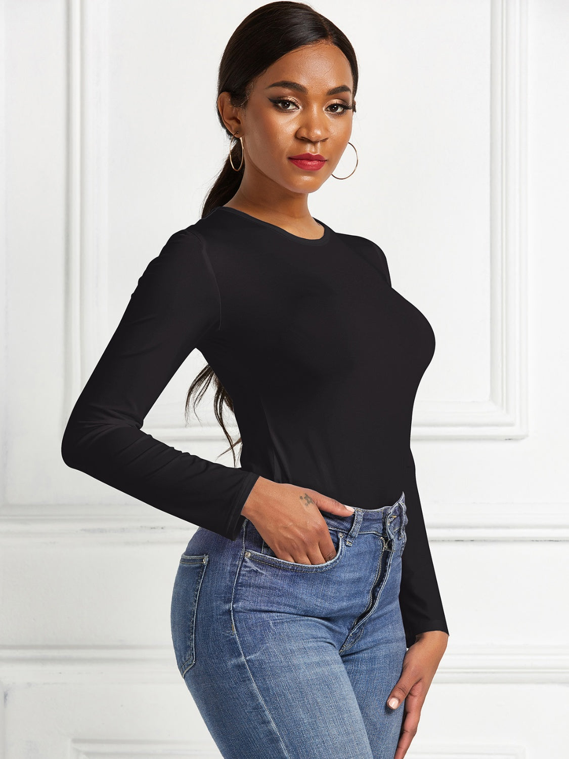 Black long sleeve ribbed bodysuit with crew neck, tucked into blue jeans.