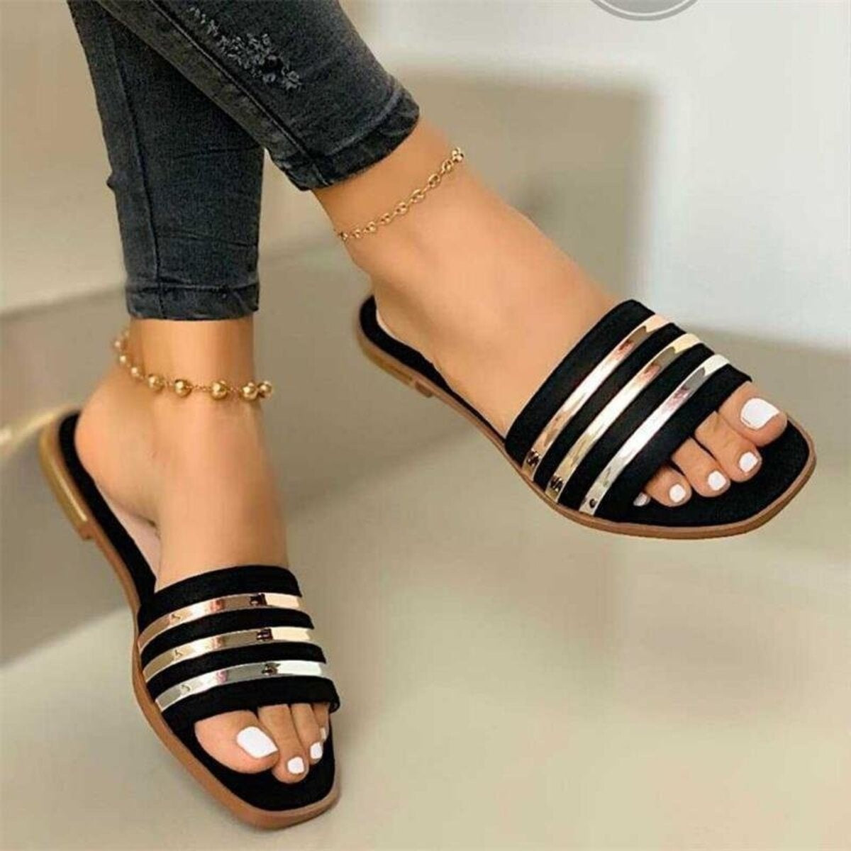 Black flat sandals with metallic stripes and open toe.