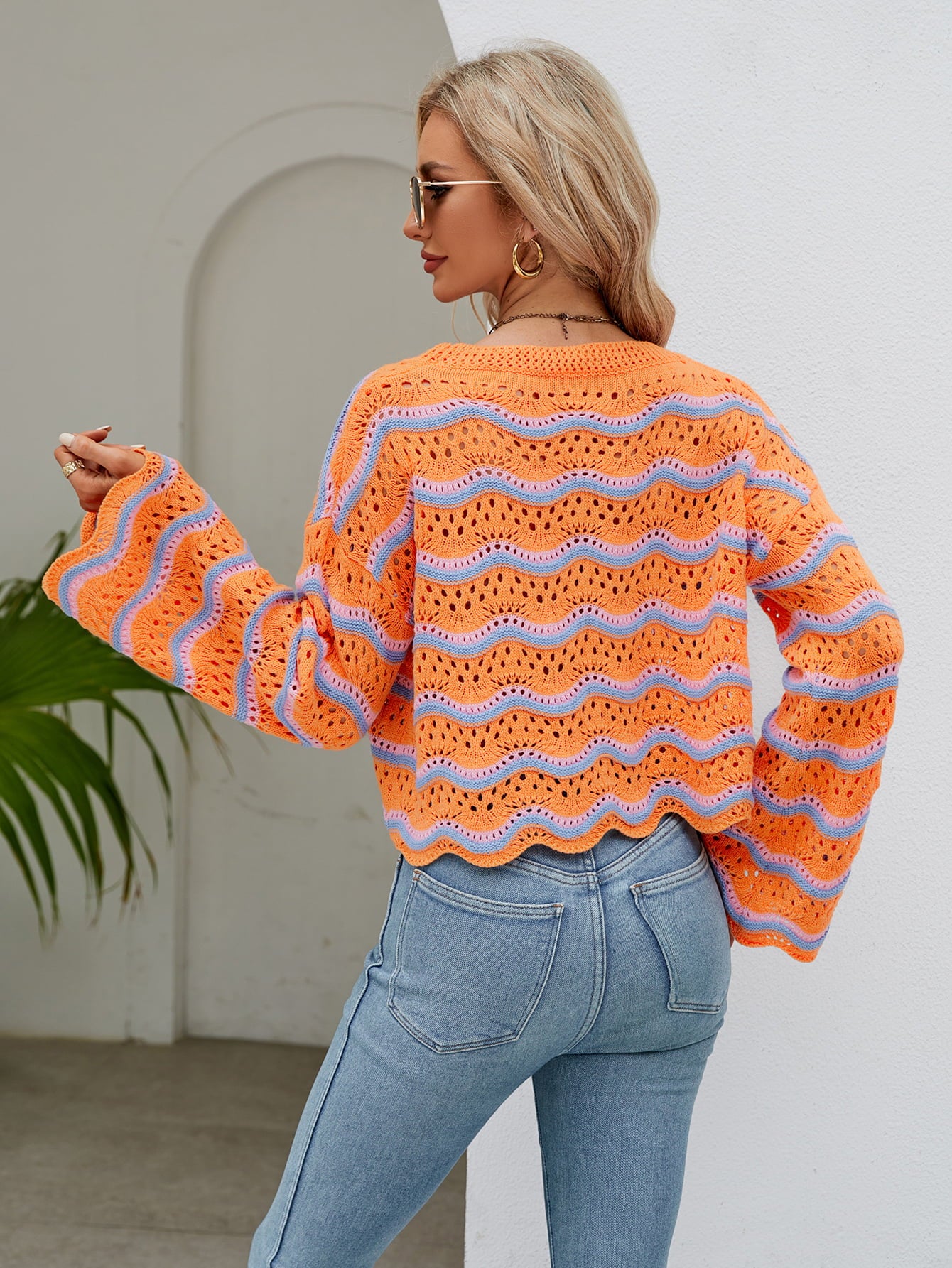 Orange-red crochet crop sweater with blue wave pattern and scalloped hem.