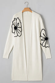 Ivory open-front maxi cardigan with black floral appliqué on sleeves.