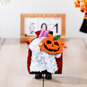 Halloween doll in sequin cape holding a pumpkin, with a black cape and white sequin dress.