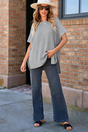 Gray ribbed knit cape sleeve top with a relaxed fit and high-low hem, styled casually.