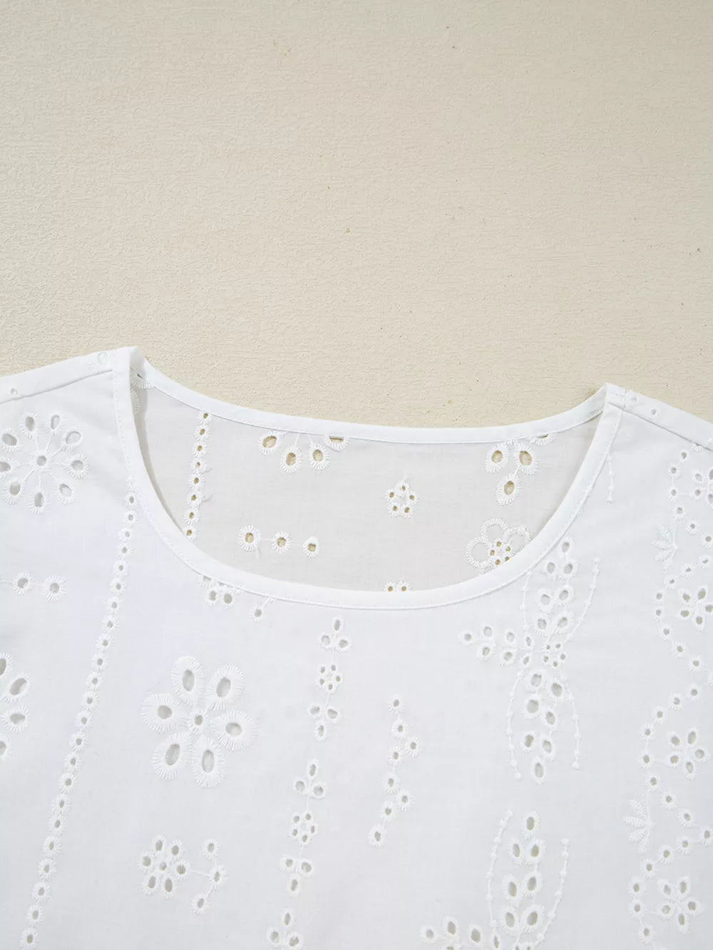 White cotton blouse with delicate eyelet embroidery and a ruffled neckline.