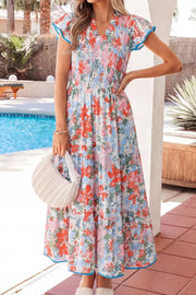 Vibrant floral maxi dress with smocked bodice, flutter sleeves, tiered skirt, and blue trim.