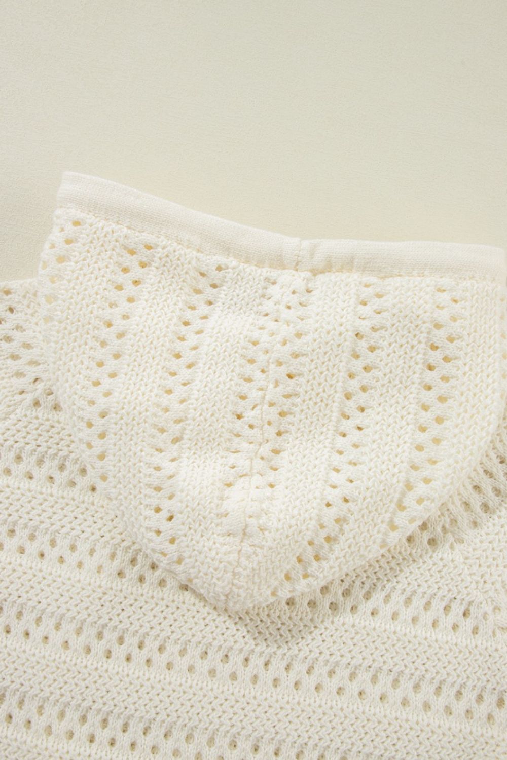 Openwork knit hoodie in beige with a drawstring detail and textured stitch pattern.