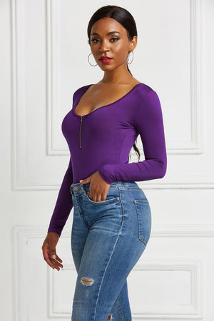 Purple long sleeve bodysuit with plunge neckline and zip front detail, styled with jeans.